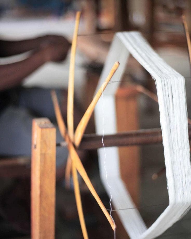 Artisan hand-spinning pure white Ahimsa Eri silk yarn on a traditional wooden charkha reel in Assam