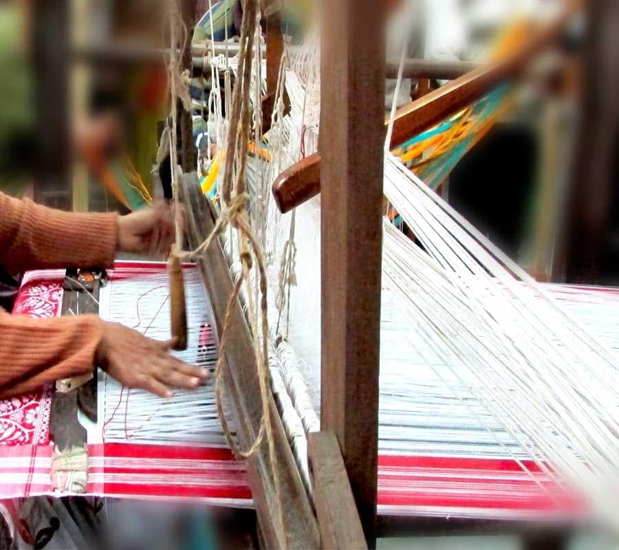 Master artisan hands operating throw-shuttle handloom with traditional Assamese extra-weft motifs